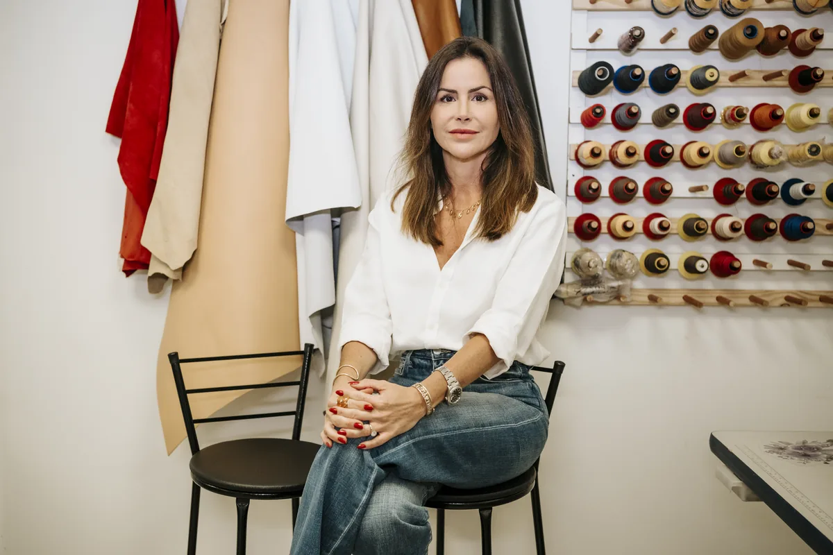 Nicole Sarantopoulos sentada no Atelier, diante dos couros e linhas