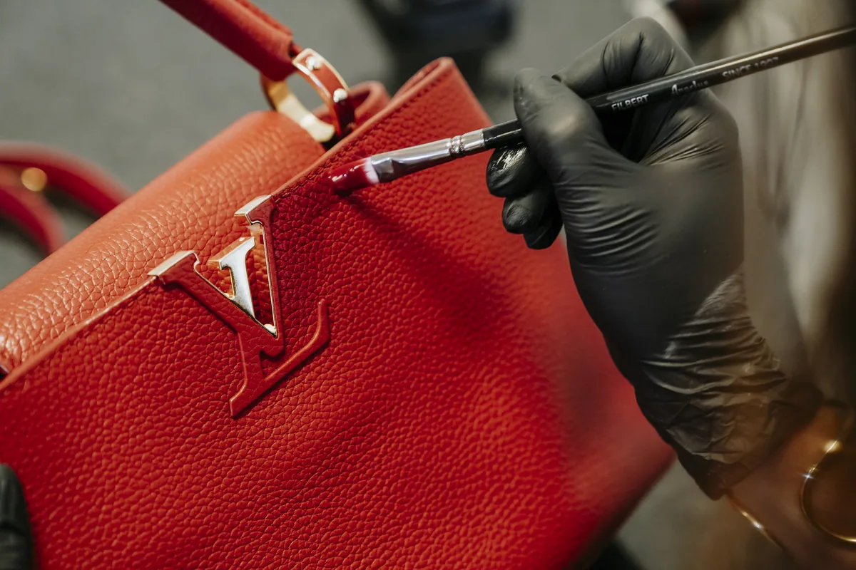 Mãos de artesã retocando o couro de uma bolsa Louis Vuitton vermelha