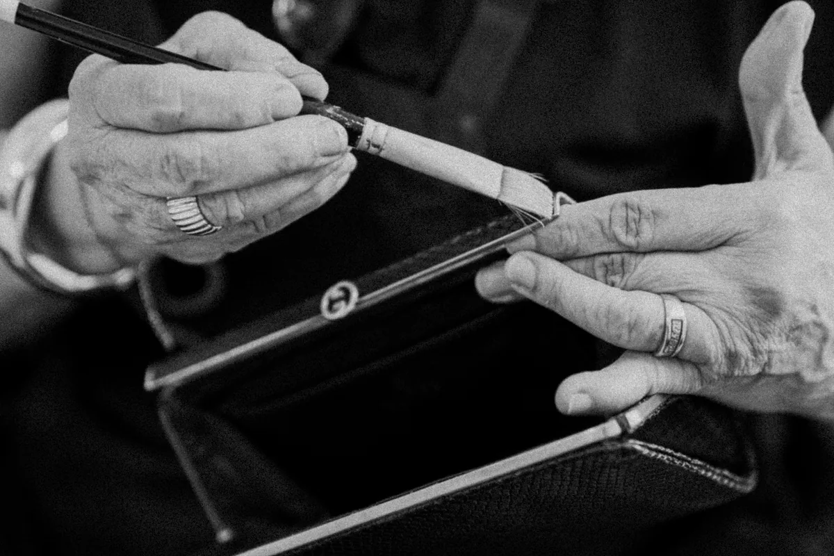 Mãos de artesã avaliando o acabamento de uma bolsa, em preto e branco