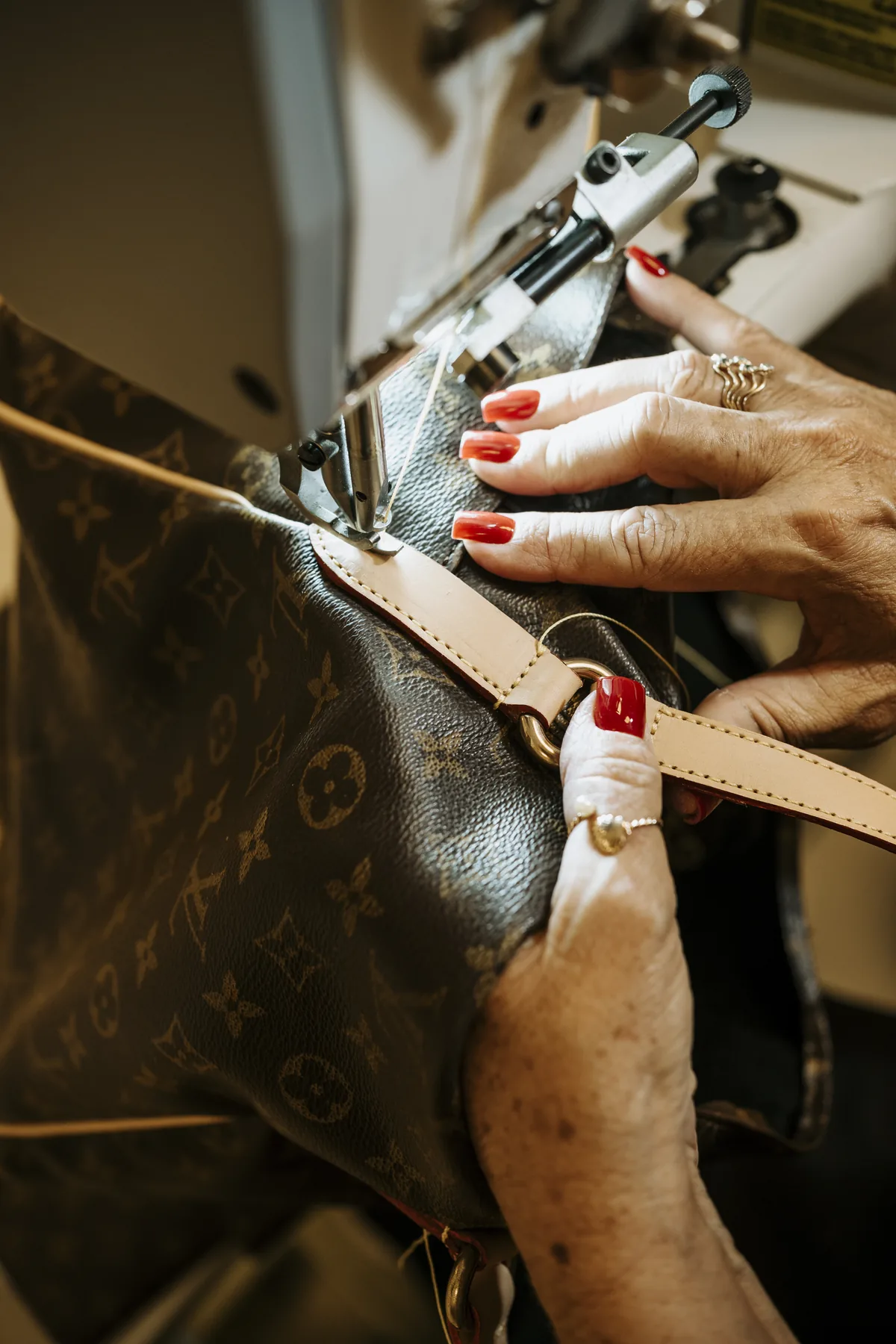Mãos costurando à máquina a alça de uma bolsa Louis Vuitton monogramada